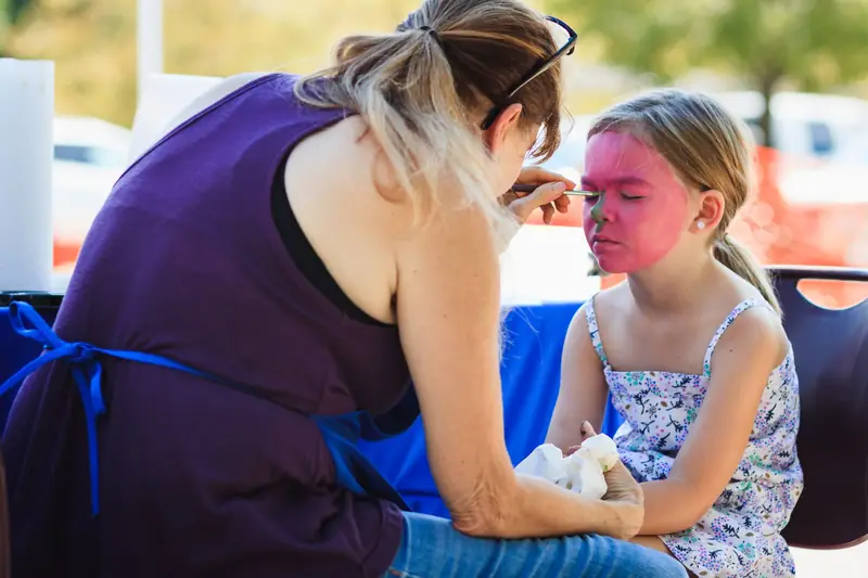 A woman painting a girl's face outdoors