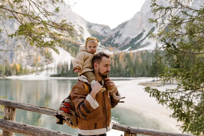 Ein Vater trägt sein Kind auf den Schultern an einem Bergsee